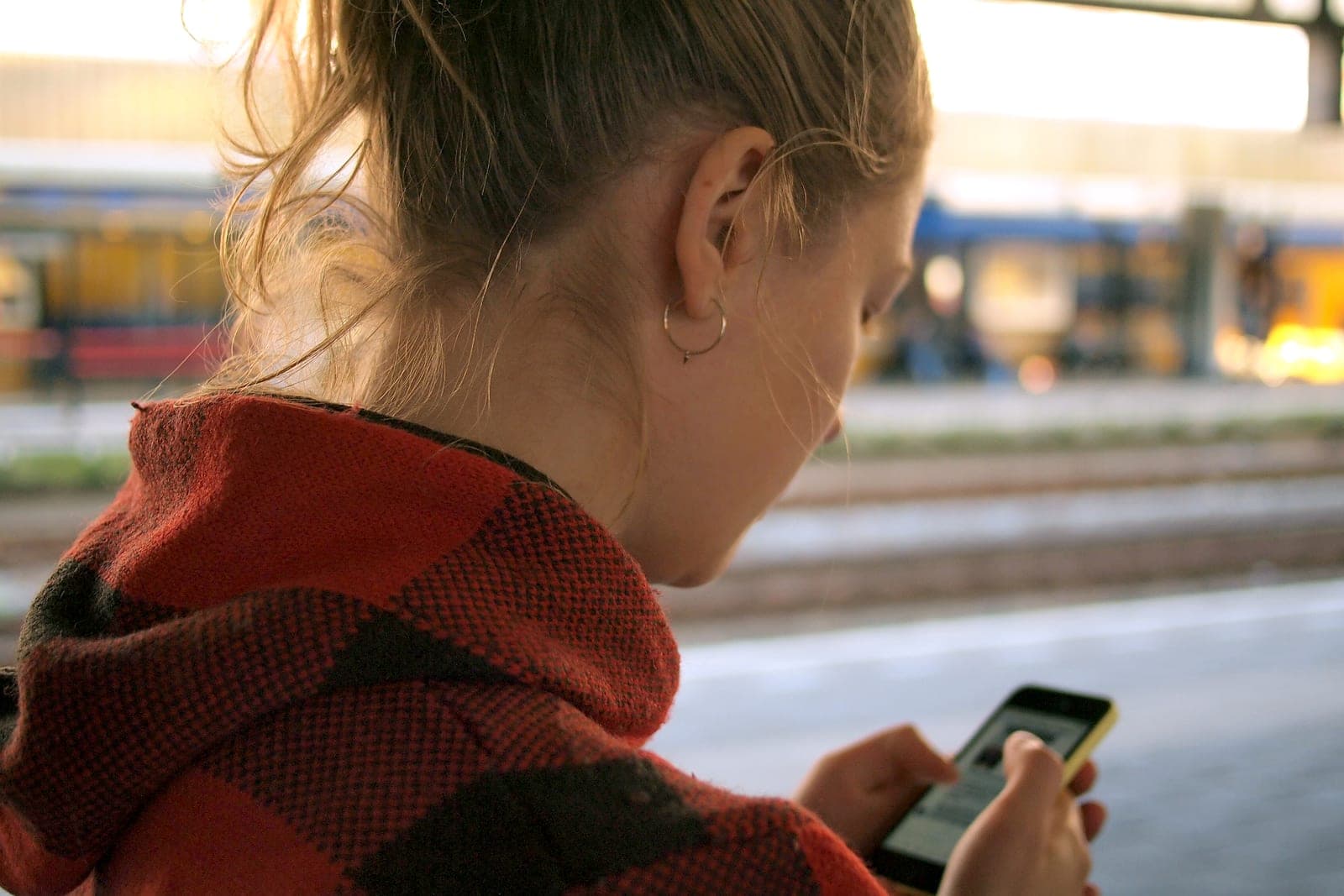 A woman in a red plaid jacket, seen from behind, reads a message on her phone
