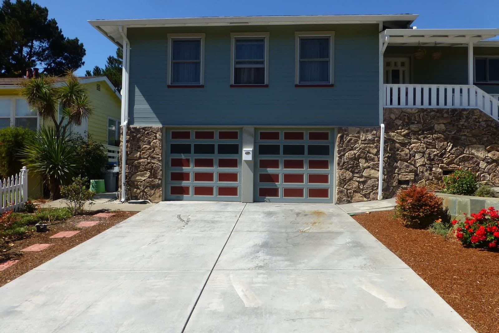A house with a two-car garage and paneled garage doors at the top of a wide concrete driveway