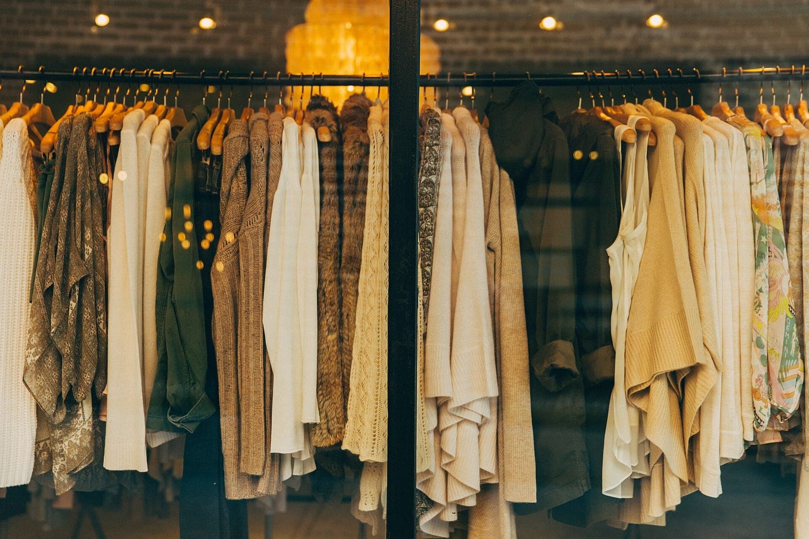 Cream, tan and olive clothing on wooden hangers along two racks in a warmly lit shop