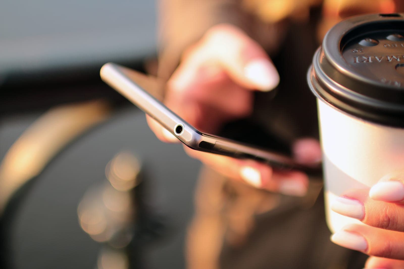 Two hands holding a smartphone next to a paper coffee cup