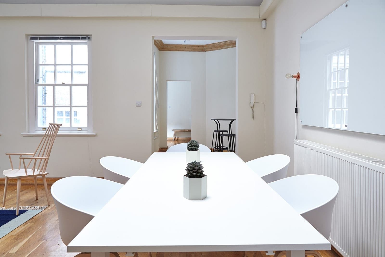 A bright meeting room with a long white table, white chairs, two small succulents and a tall window