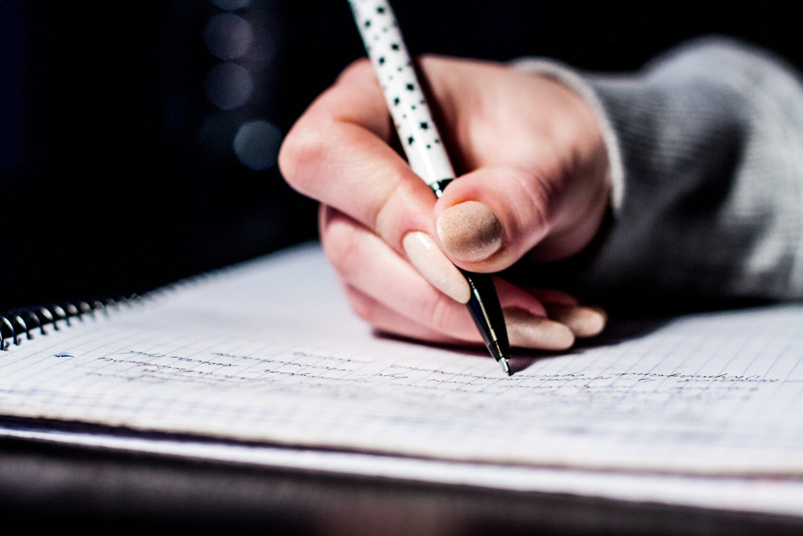 A hand writing notes in a spiral notebook with a pen