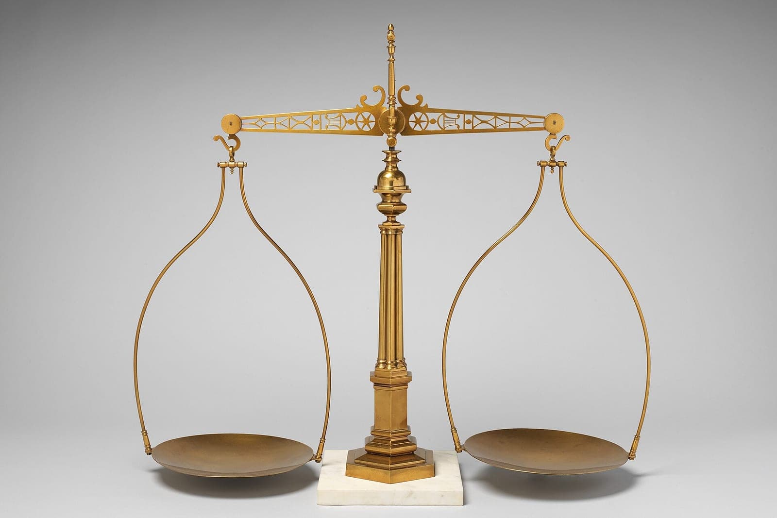 A brass balance scale with two empty pans on a white marble base