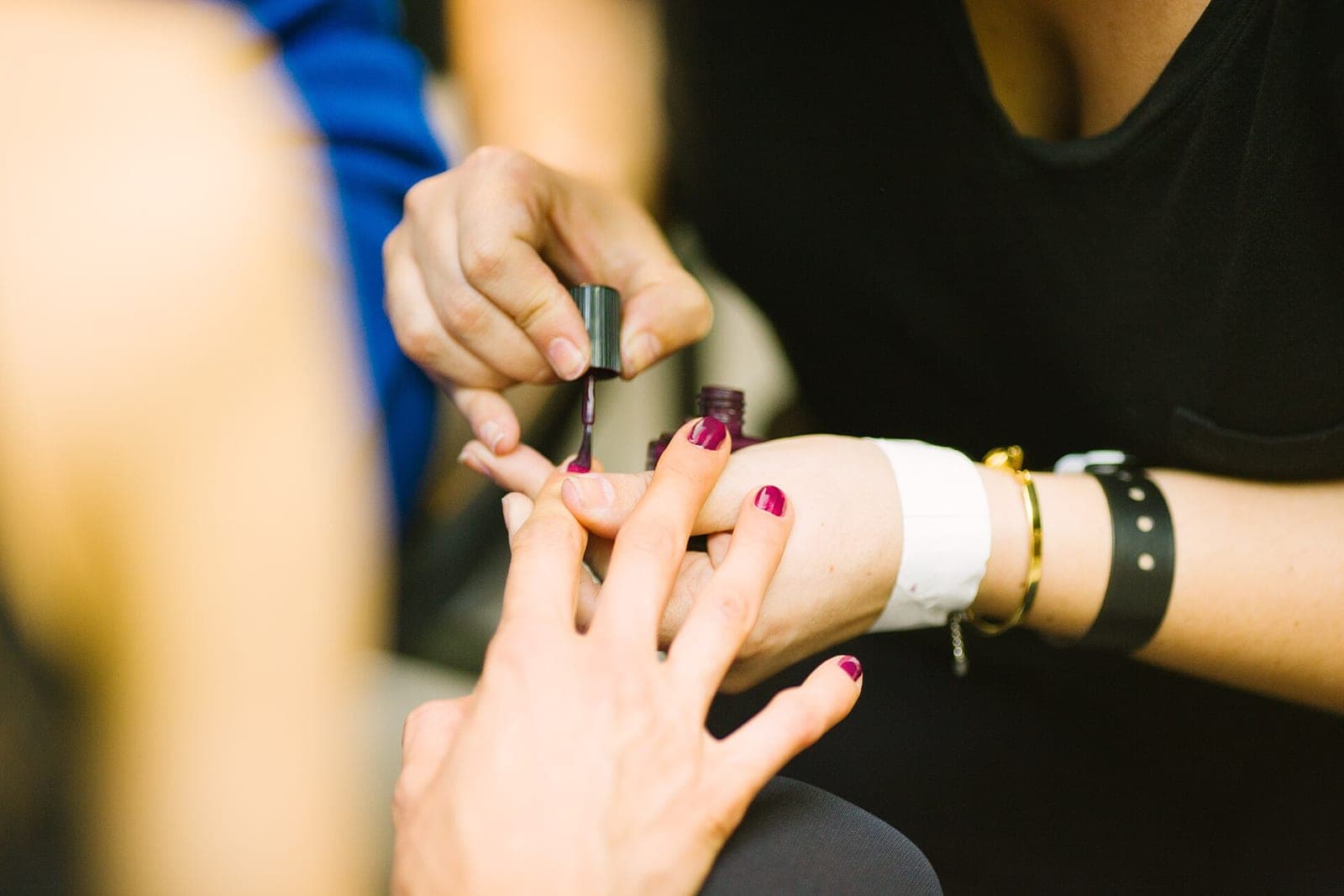 Close-up of a nail technician's hands brushing deep plum polish onto a client's fingernails