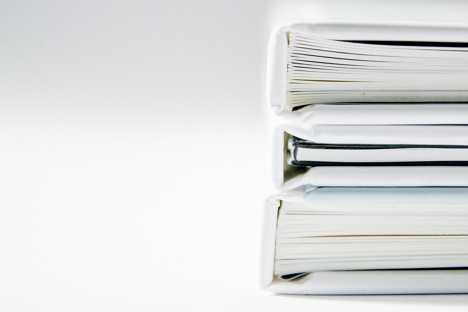 Three white ring binders full of paper stacked on a white table