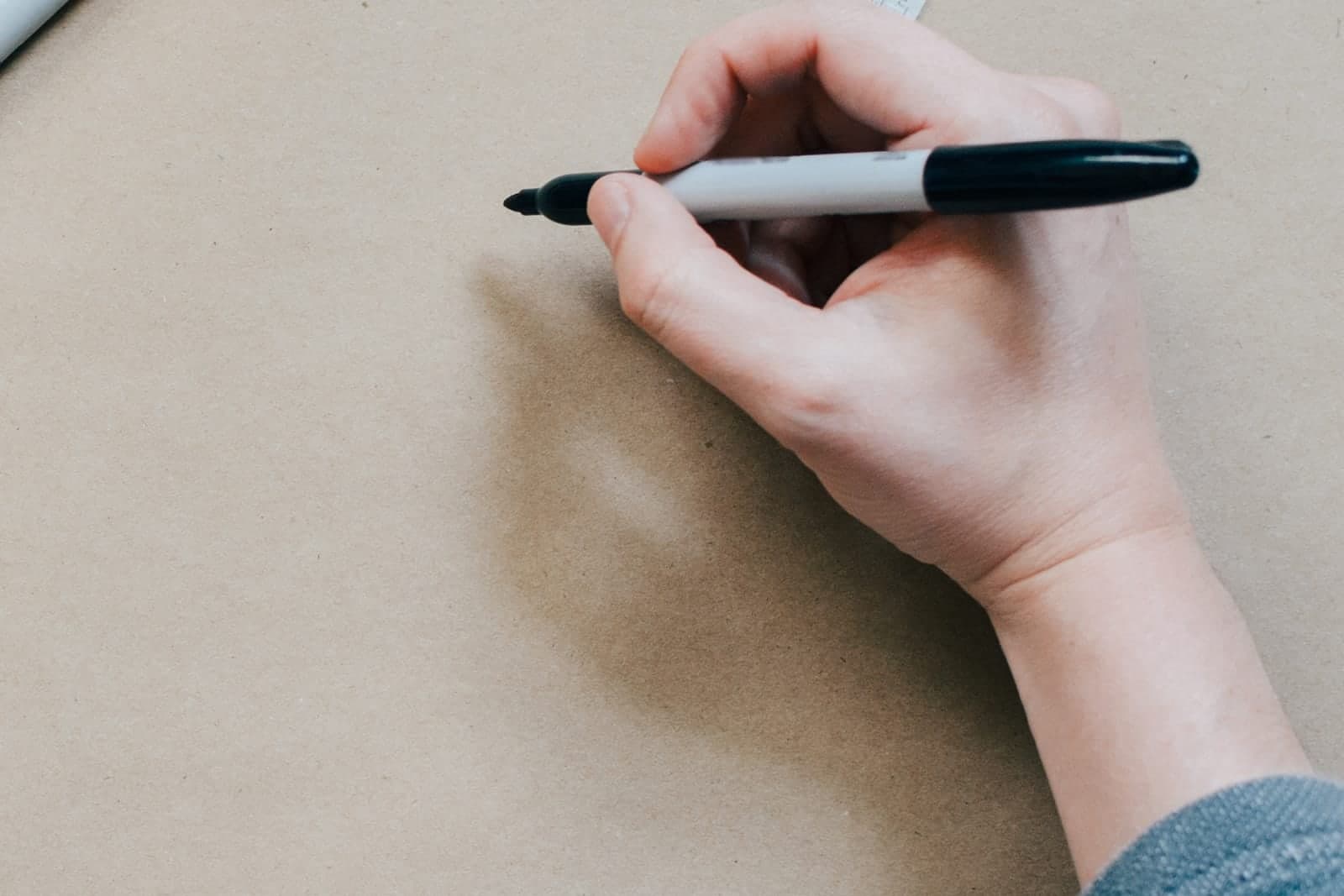 A hand holds a black marker over a large sheet of brown paper, ready to sketch