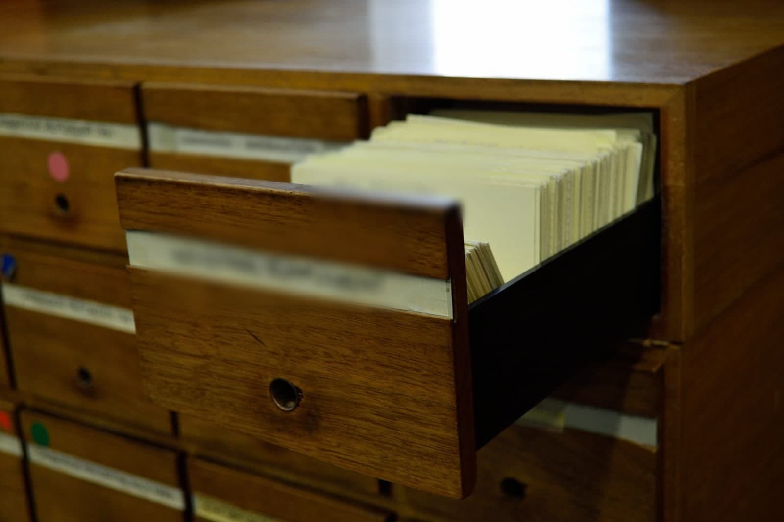 An open wooden card file drawer packed with index cards