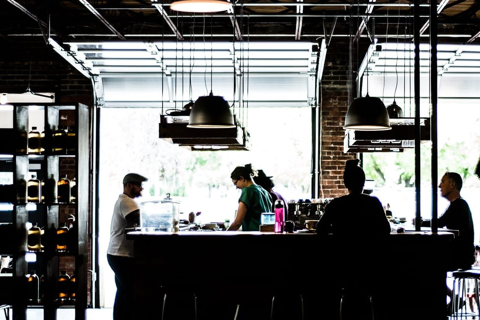 Staff and customers at a long counter in a bright coffee house with open garage doors