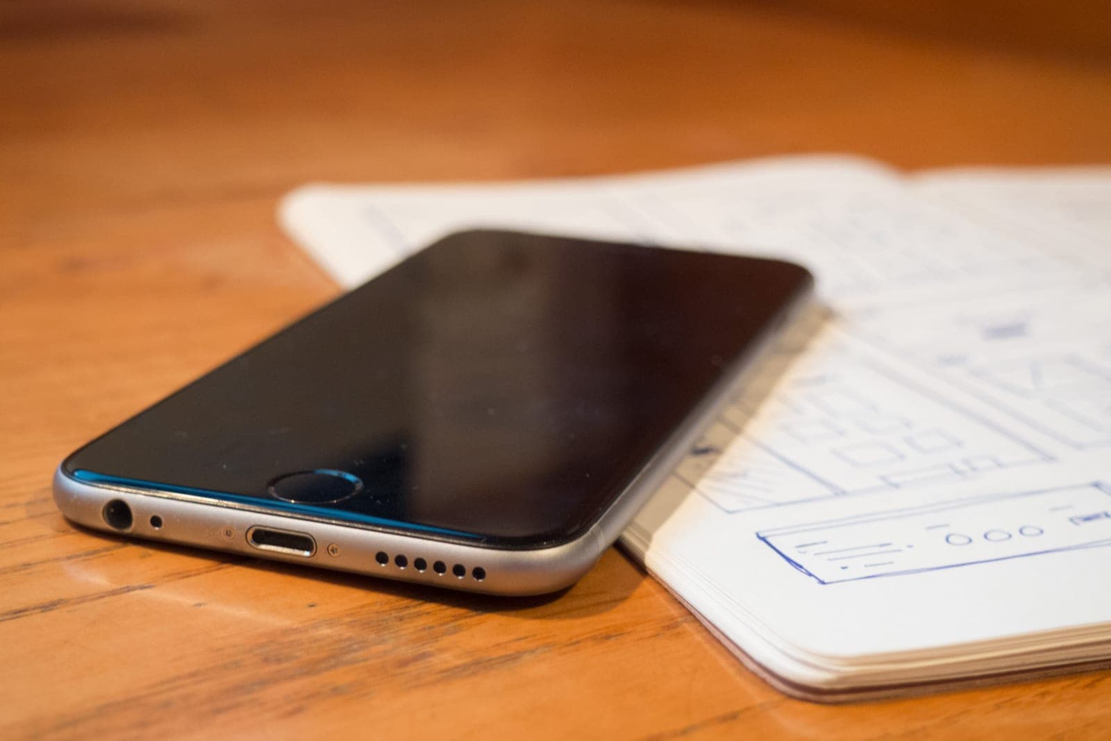 A smartphone resting beside a notebook of hand-drawn app screen sketches on a wooden table