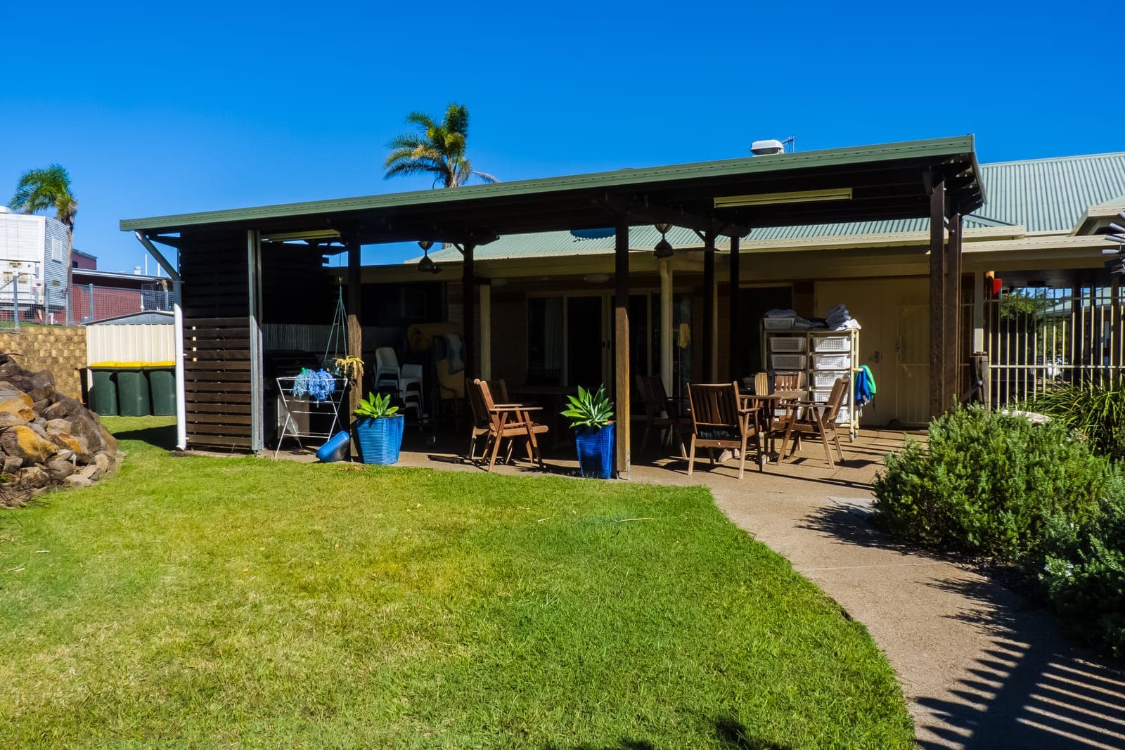 A single-story care residence with a covered patio, wooden chairs and potted plants beside a sunny lawn