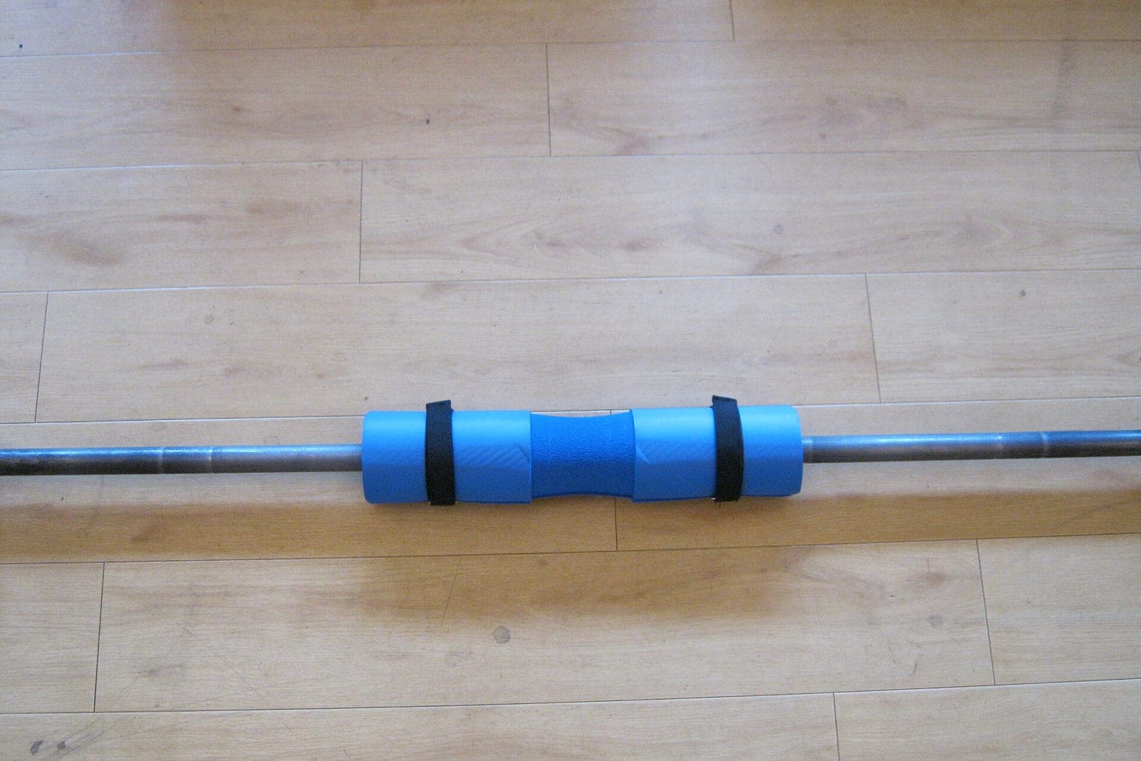 A barbell with a blue foam pad lying on a light wood floor