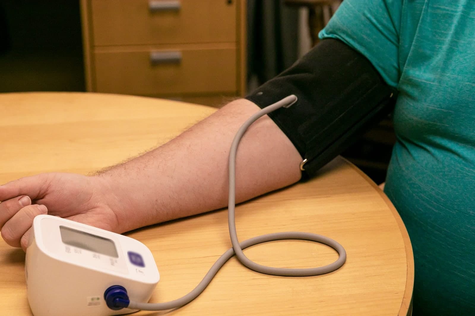 A blood pressure cuff on a person's arm beside a digital monitor on a wooden table