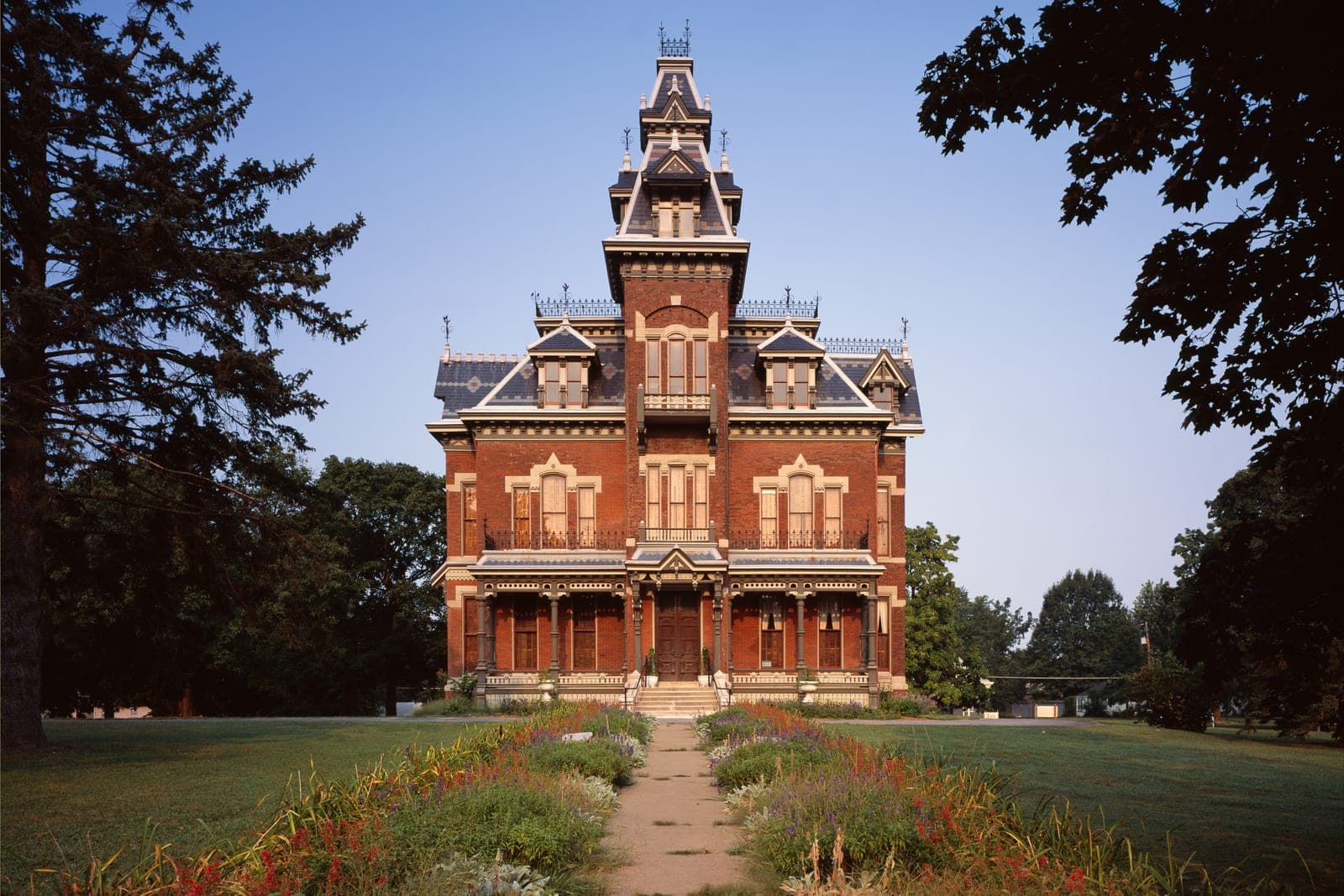 The red-brick Vaile Mansion and its tall tower at the end of a flower-lined path in Independence, Missouri