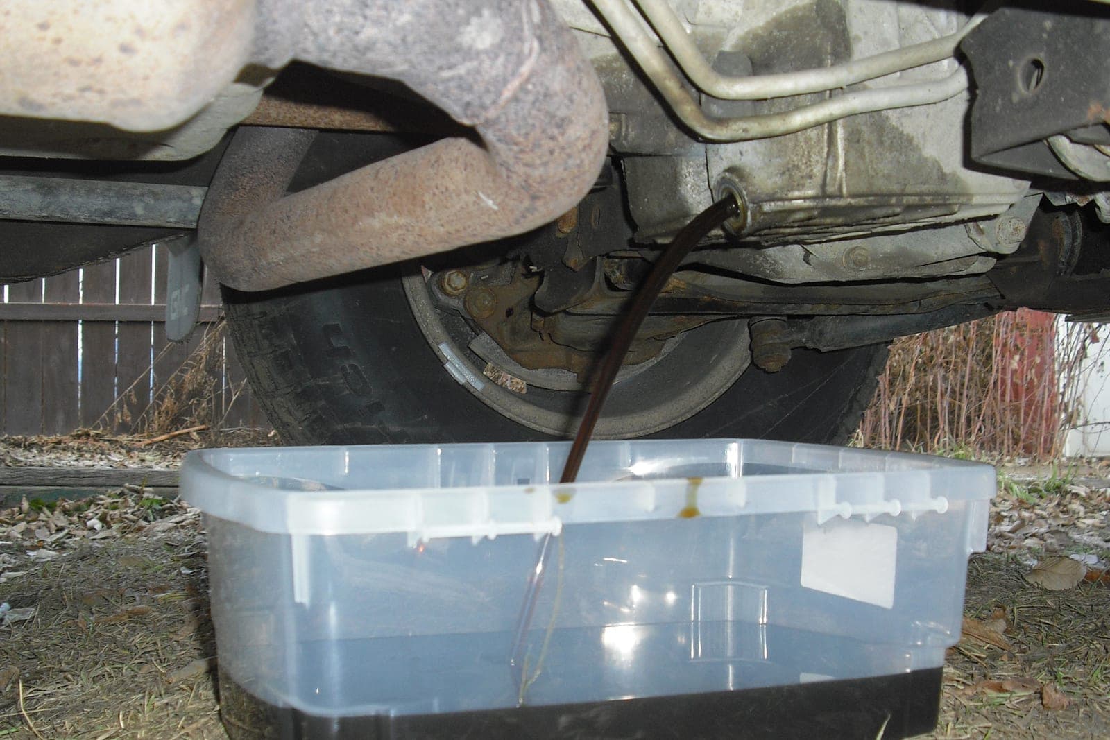Used engine oil drains from under a vehicle into a plastic tub