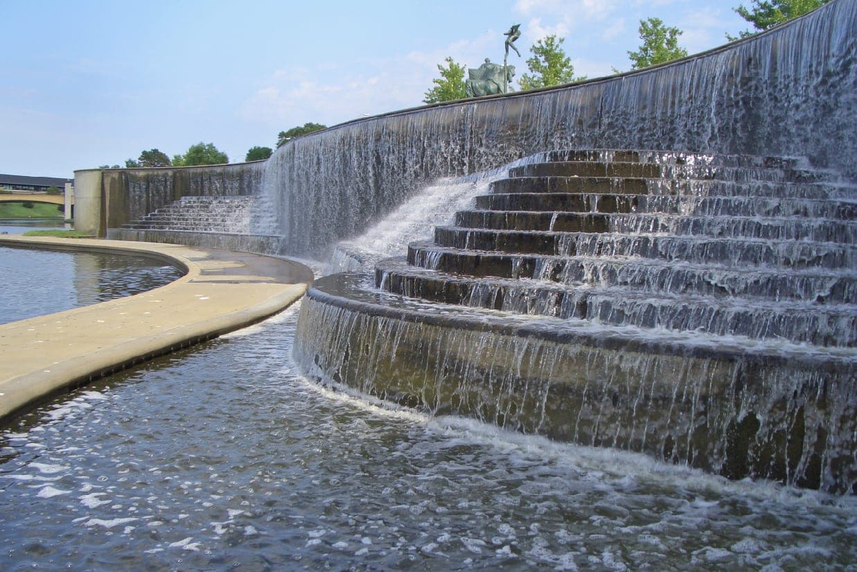 Water spills over the curved stone steps of the Volker Fountain basin along Brush Creek in Kansas City, Missouri