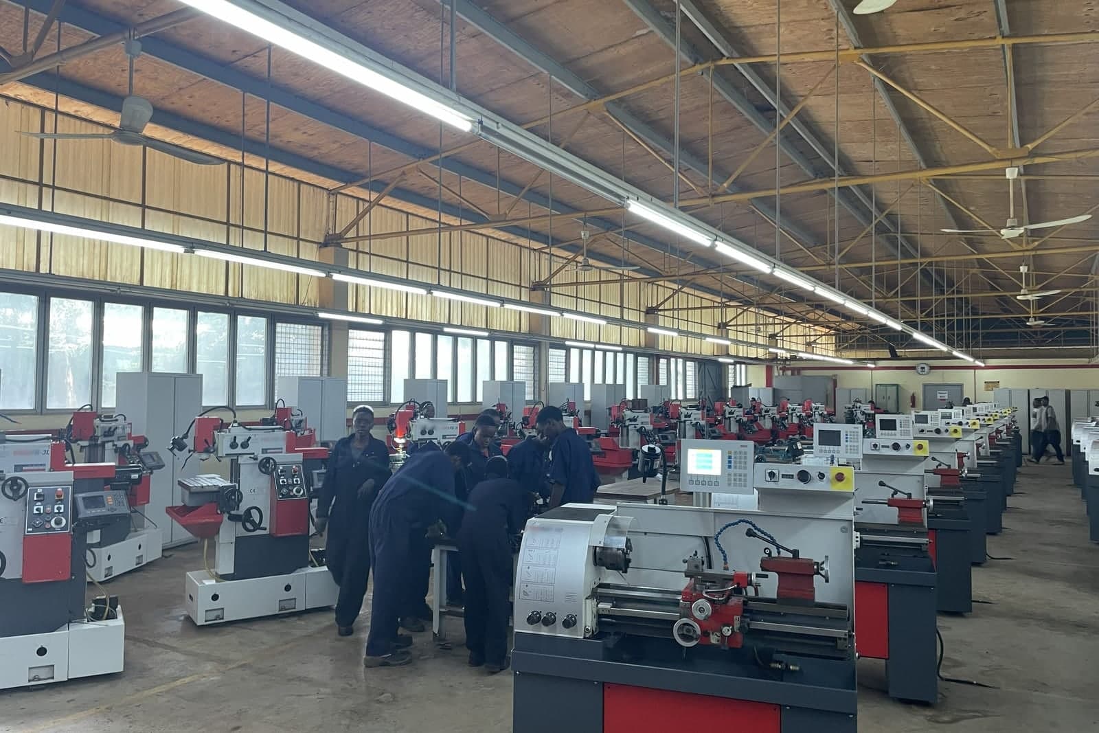 Rows of new lathes and milling machines fill a bright machining workshop, with workers in blue coveralls at a bench