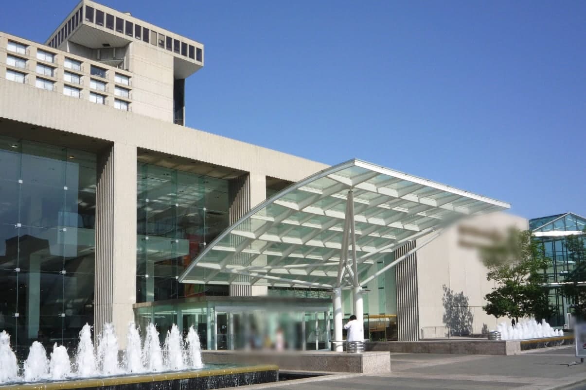 A glass canopy over the shops entrance at Crown Center, with fountains in front and a blue sky, in Kansas City, Missouri