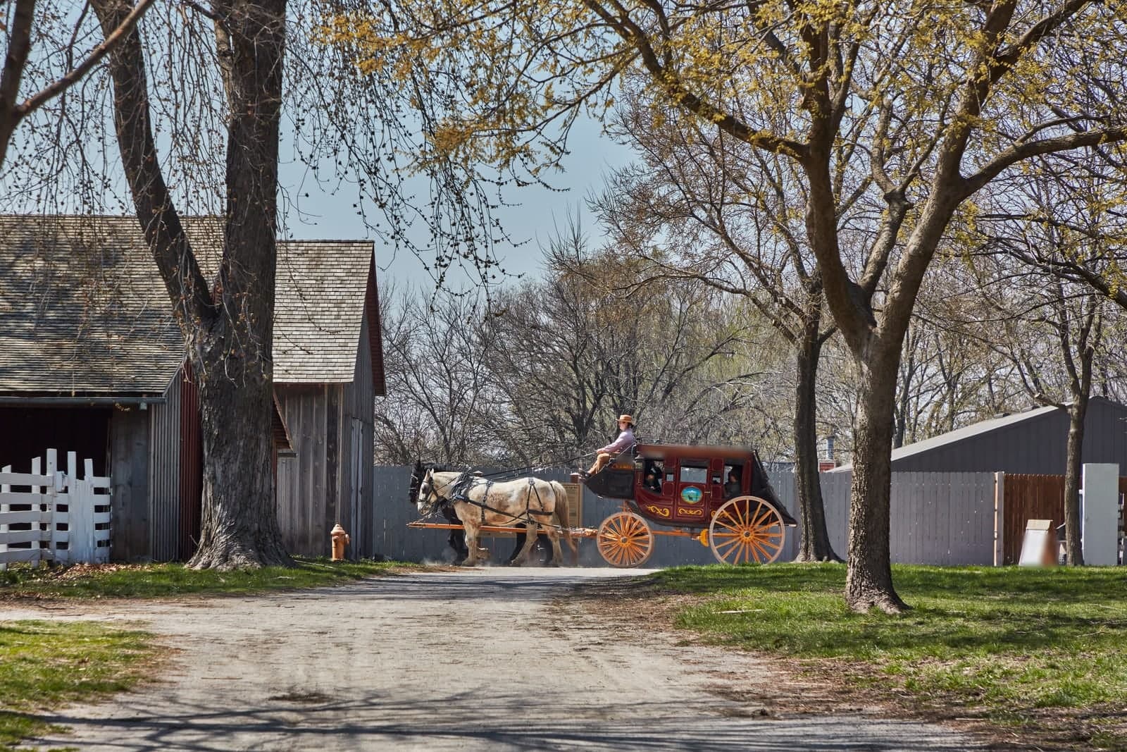 A horse-drawn red stagecoach rolls past barns and trees at the Mahaffie Stagecoach Stop and Farm in Olathe, Kansas
