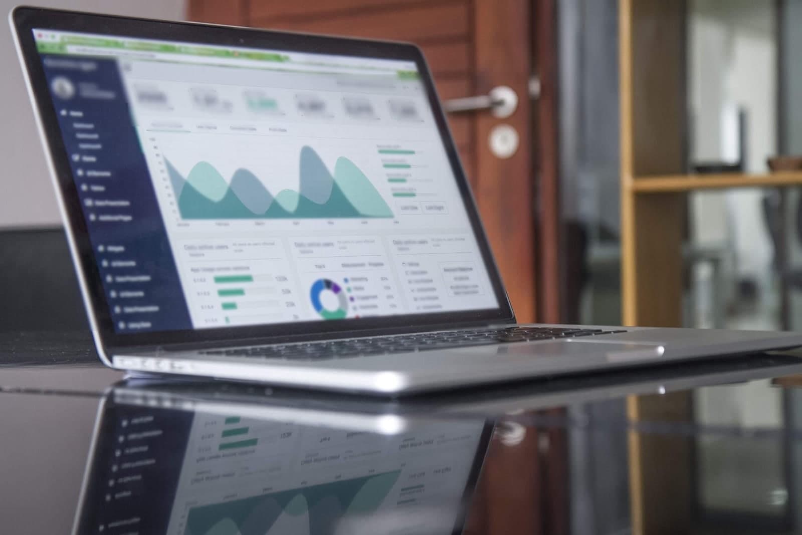 A laptop on a glossy table shows a dashboard of charts and graphs