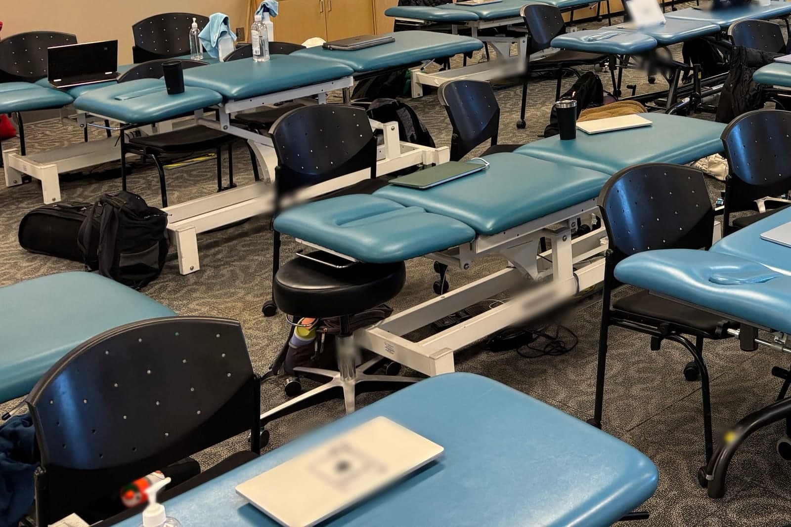 Rows of teal treatment tables and black chairs in a bright physical therapy room
