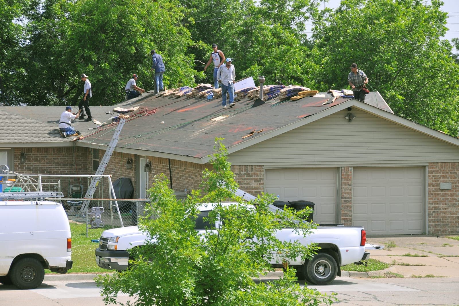 A roofing crew lays new underlayment and shingle bundles on a house roof