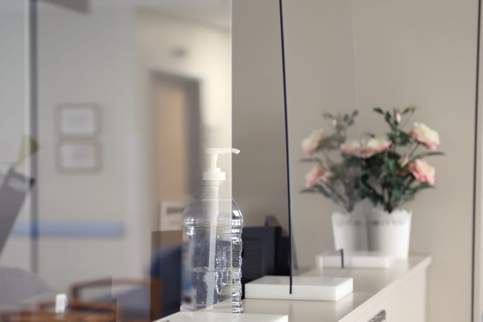 A clinic front counter with clear shields, hand sanitizer and two white pots of pink flowers
