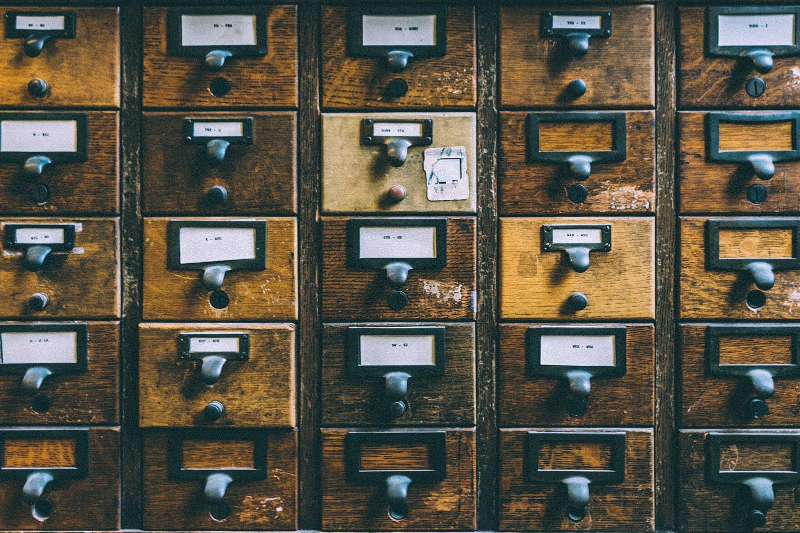 Rows of old wooden card catalog drawers with metal handles and small paper labels