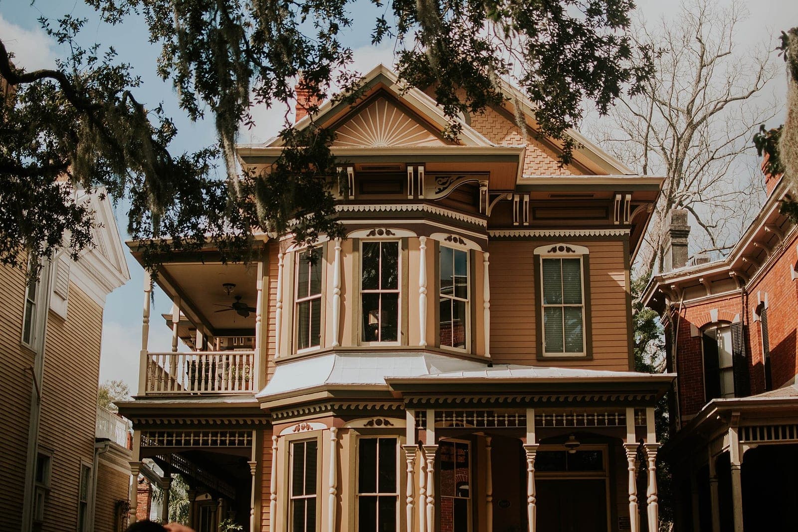 A large old house with a deep porch and bay windows under the branches of a tree