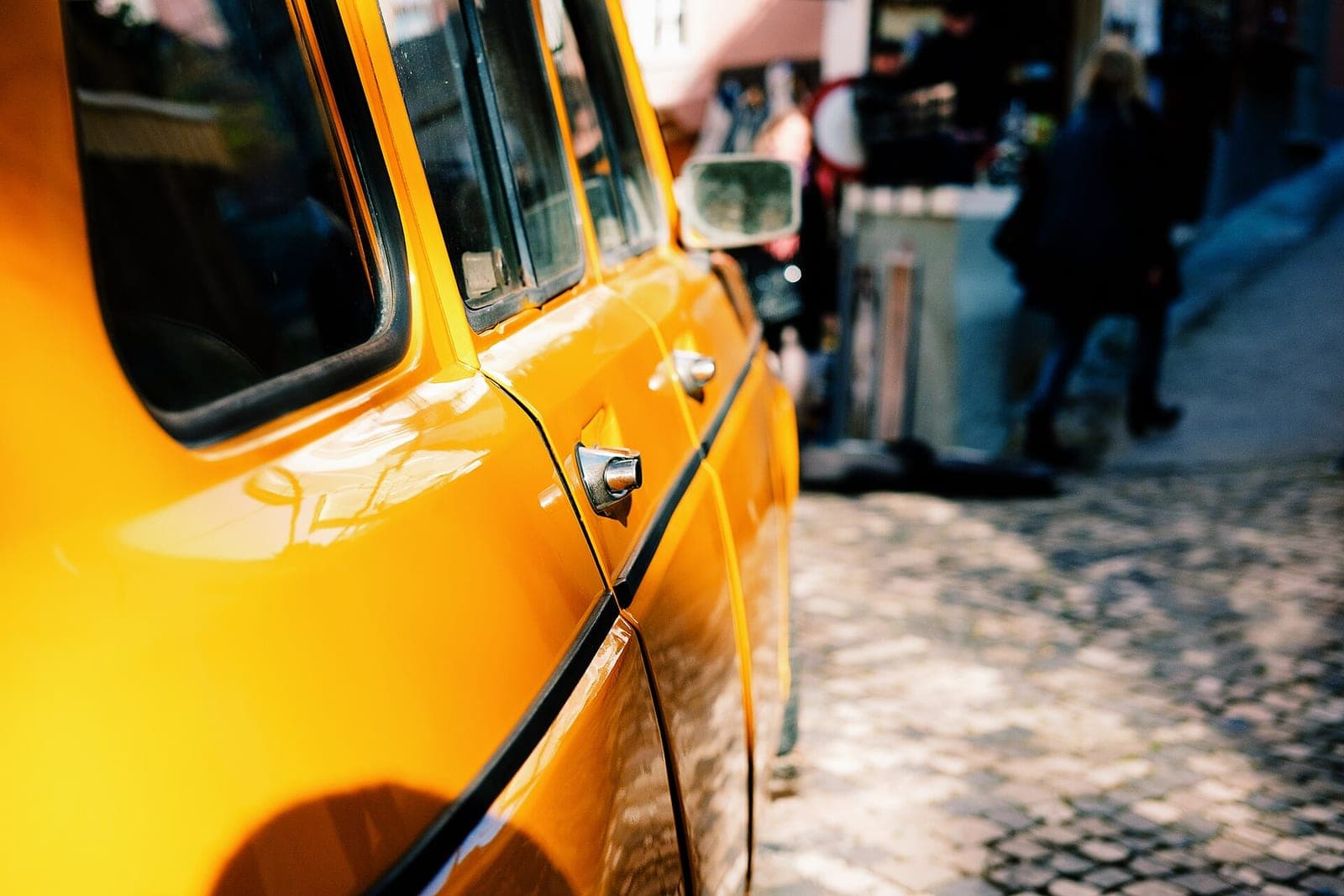 The side of a bright yellow car parked on a sunny cobblestone street