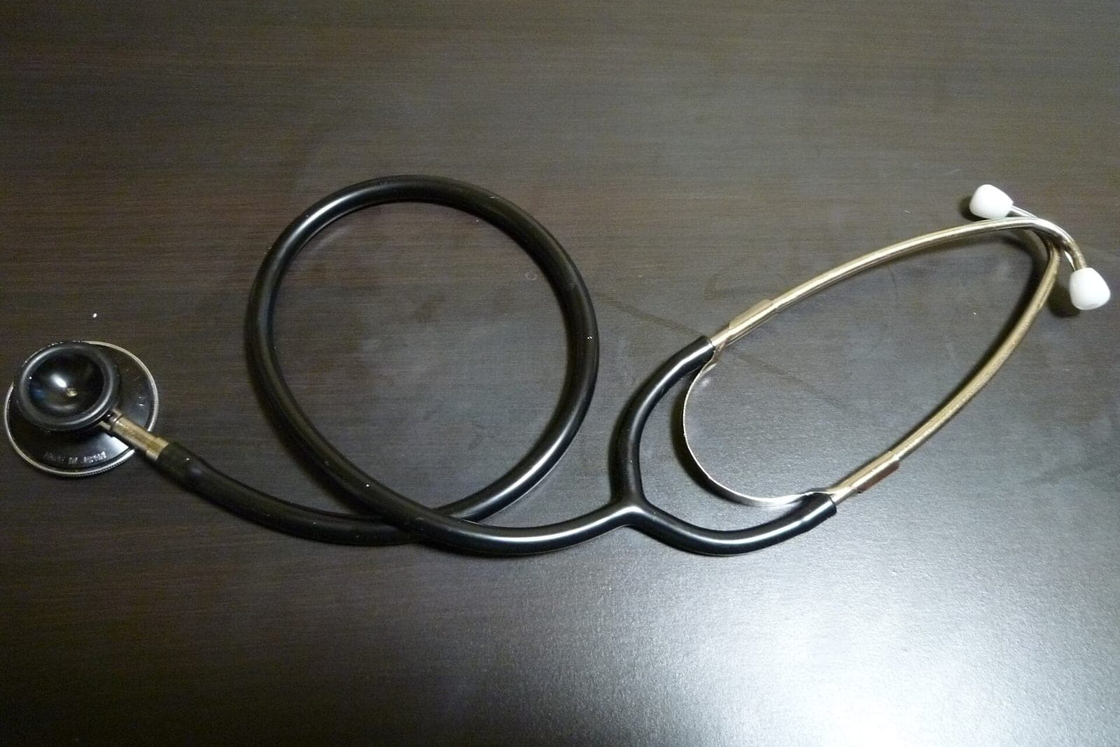 A black stethoscope with silver ear tubes lying on a dark wooden desk