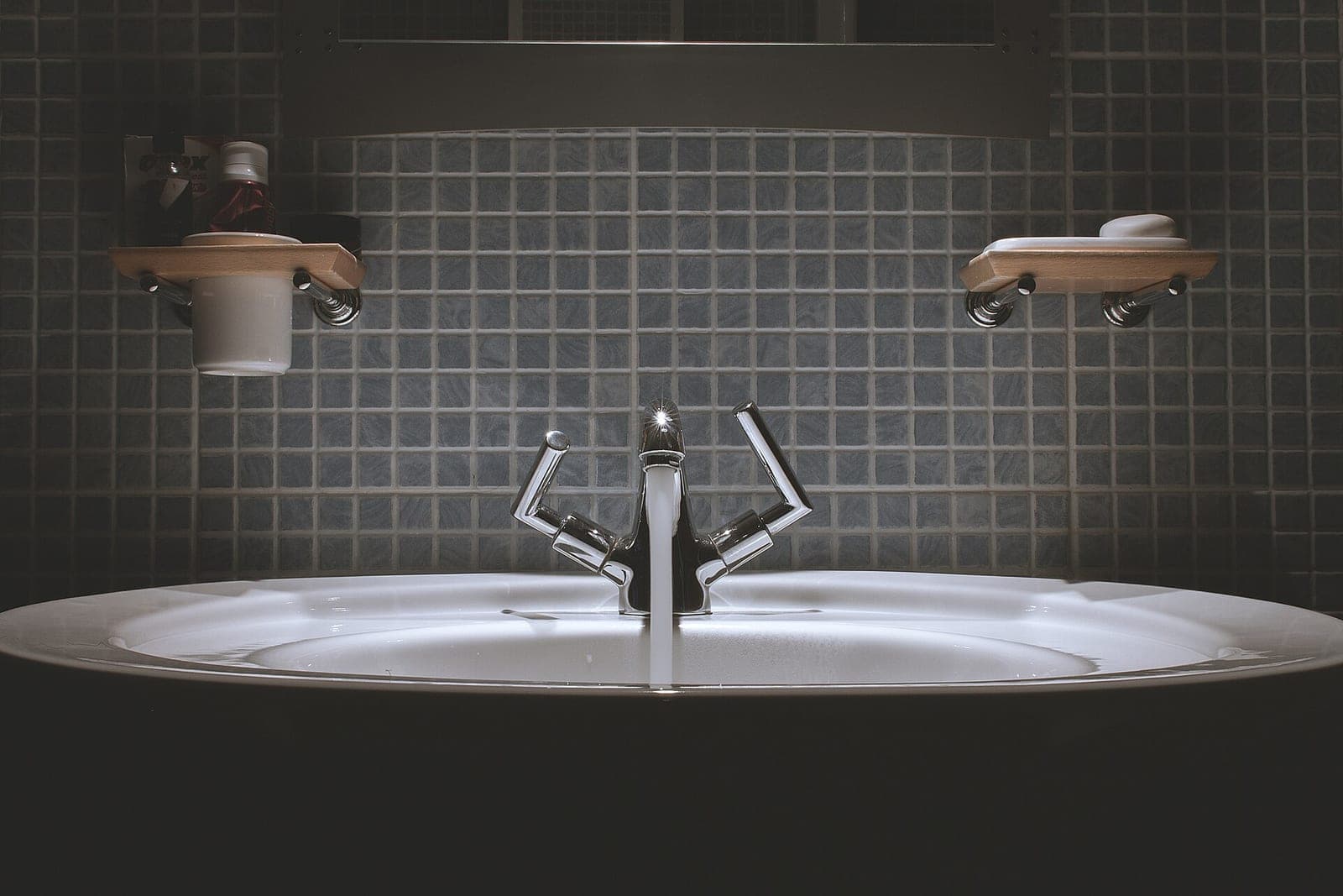 A bathroom sink with a chrome faucet running against dark gray tile