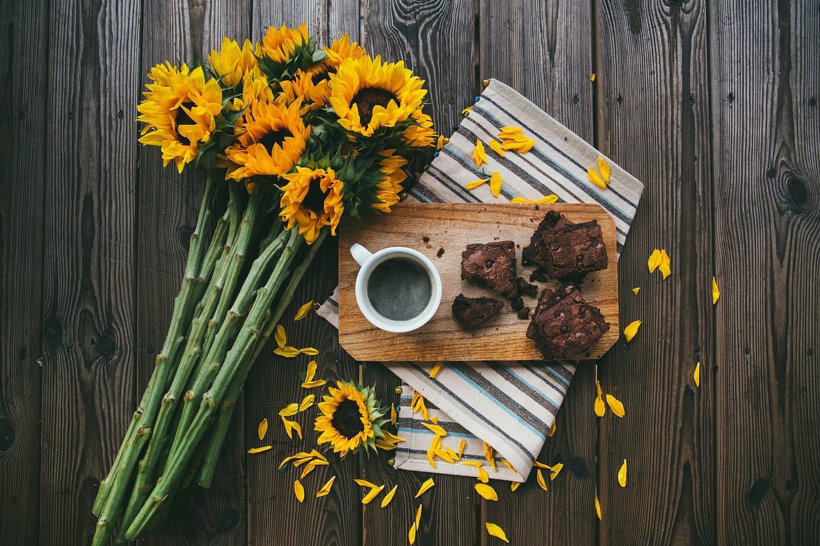 Sunflowers, a cup of coffee and brownies on a wooden board on a dark wooden table