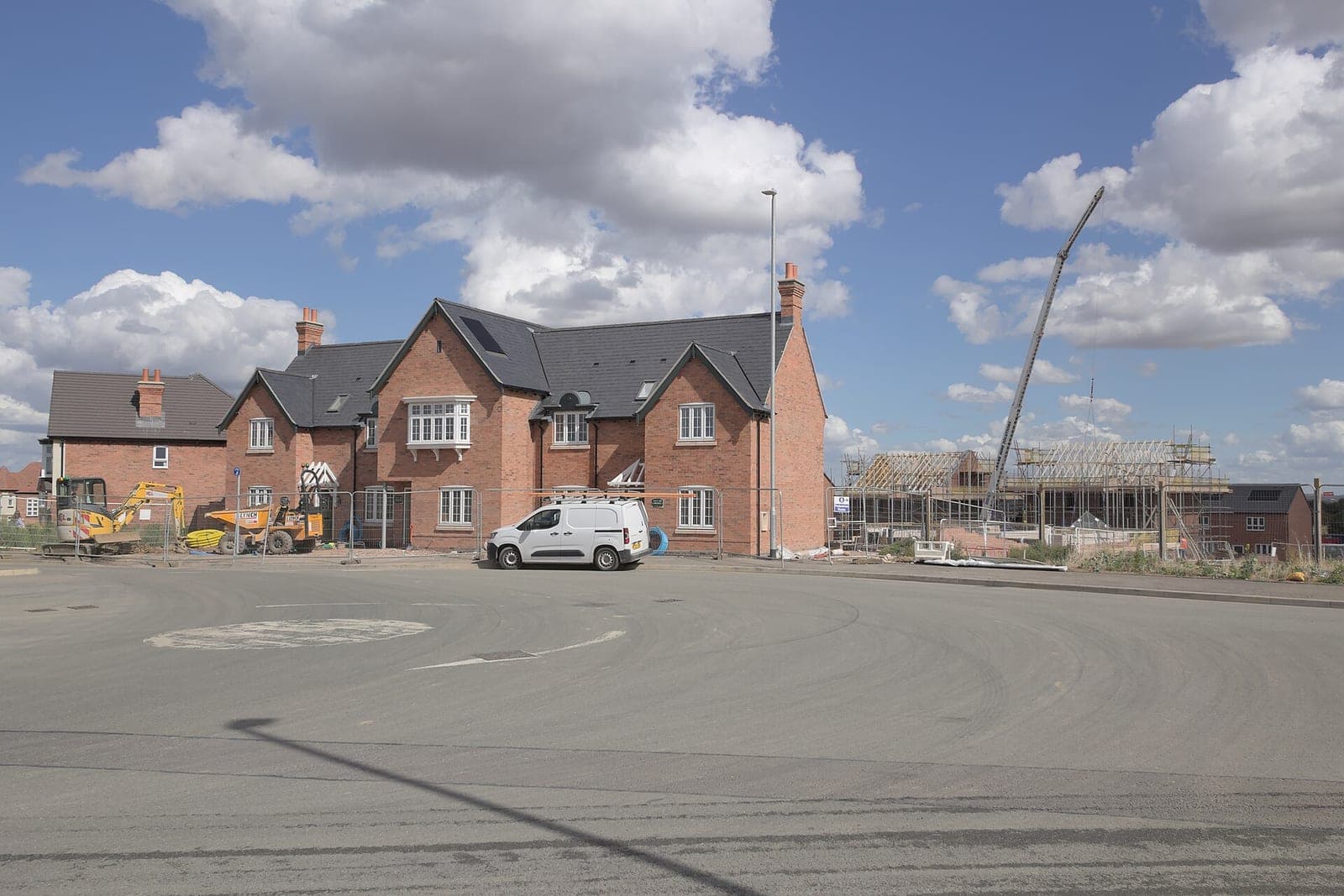 New brick houses and timber roof frames going up on a residential building site with a small excavator and a white van