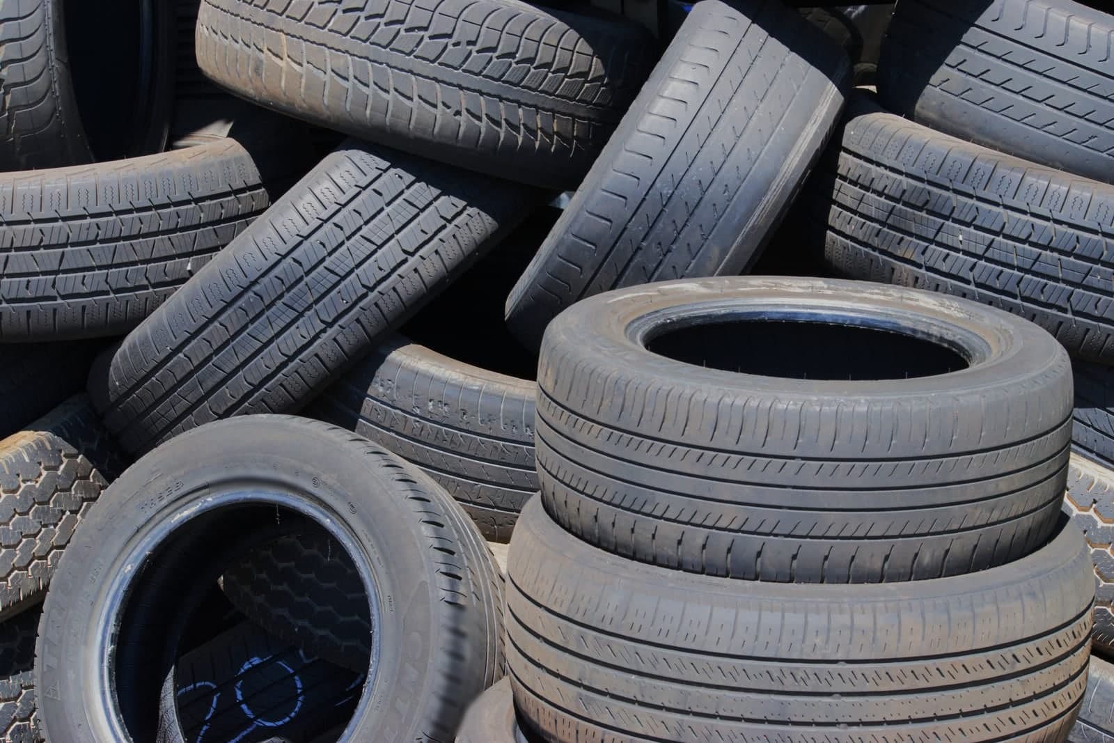 A pile of used car tires stacked in bright daylight