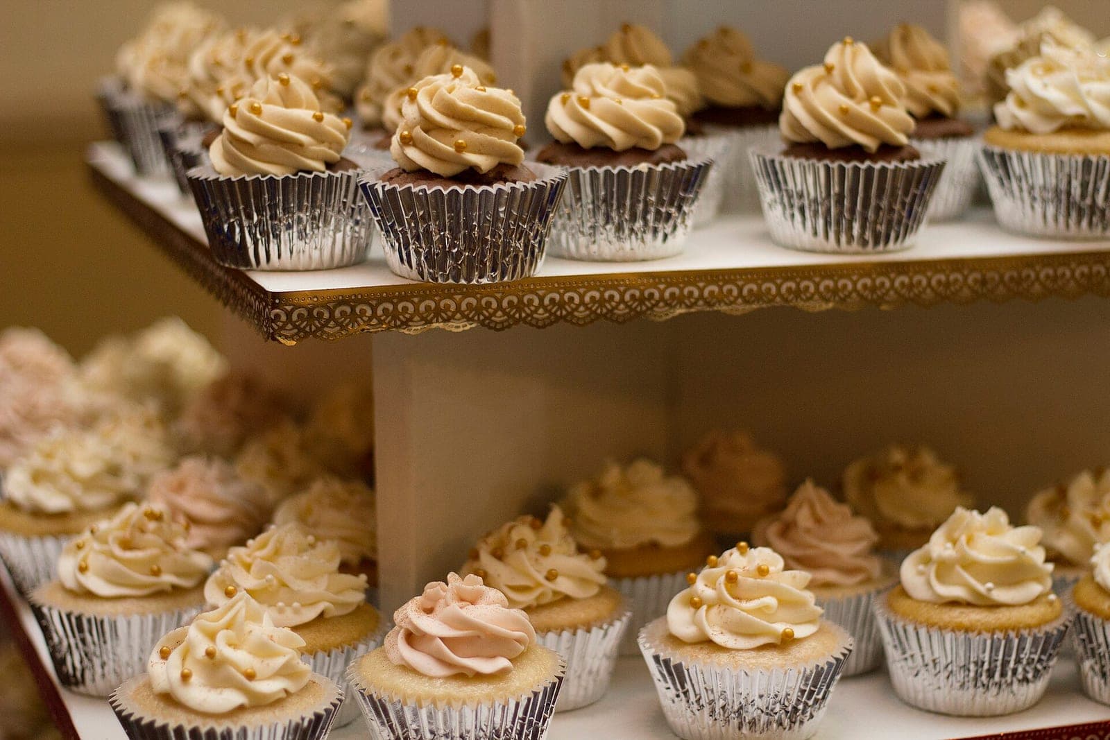 Frosted cupcakes in silver wrappers fill two shelves of a white tiered stand
