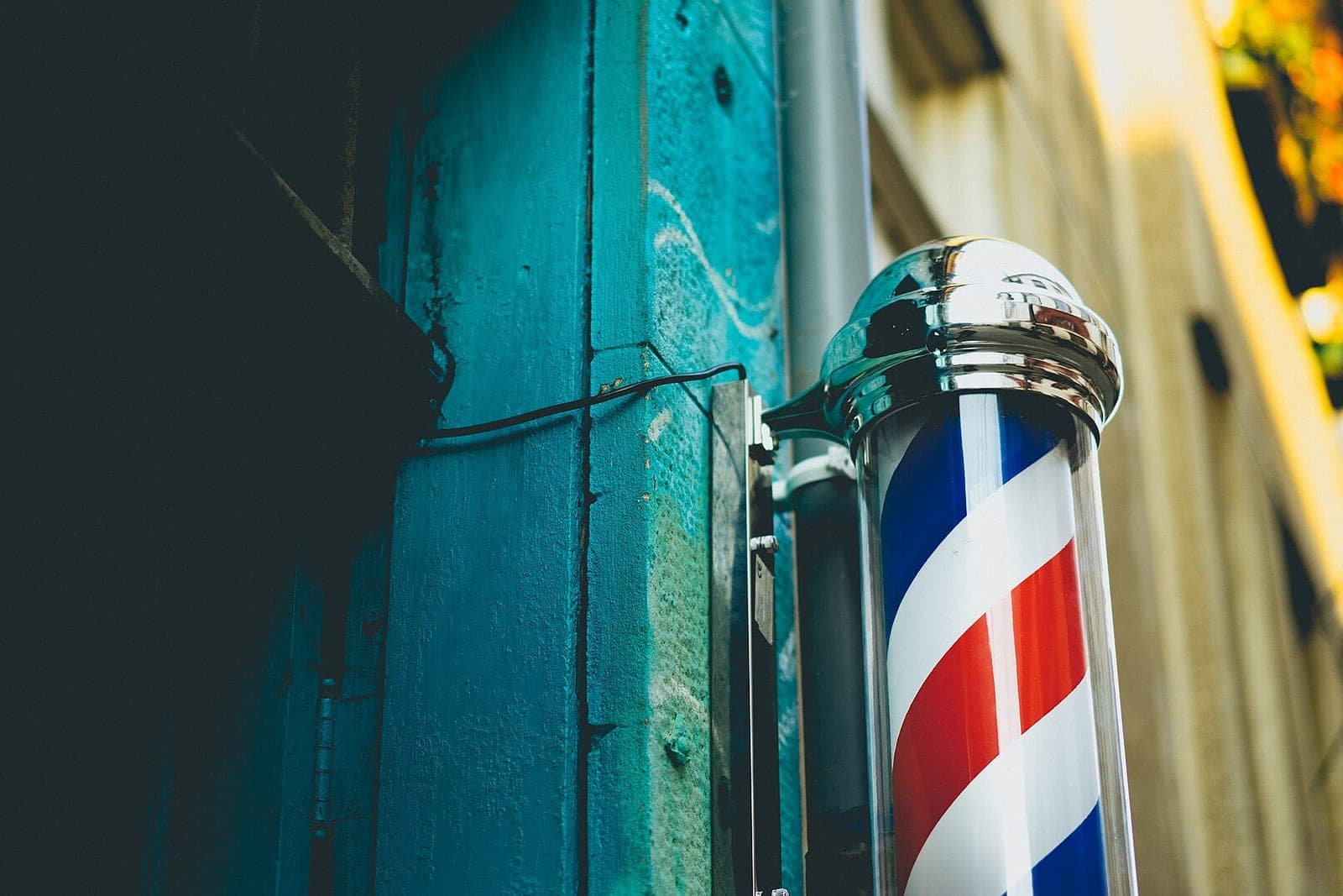 A red, white and blue striped barber pole with a chrome cap mounted beside a teal doorway