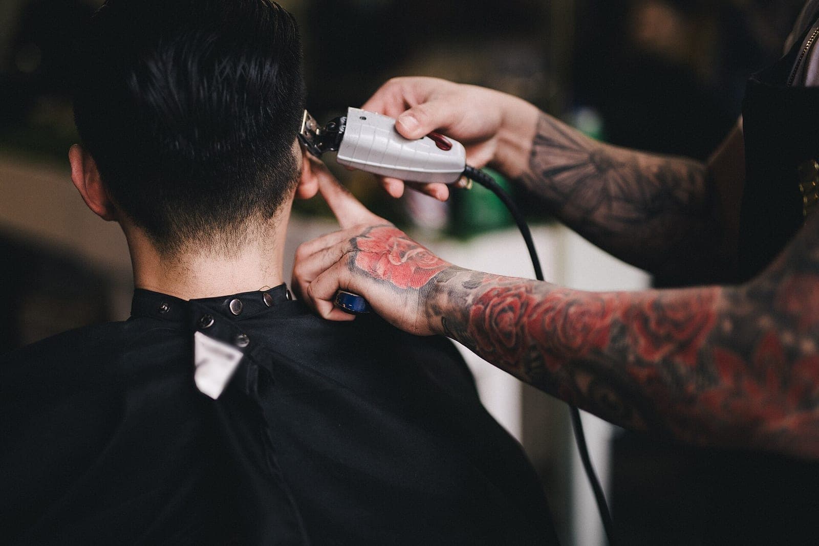 A barber's hands run electric clippers up the back of a seated client's neck