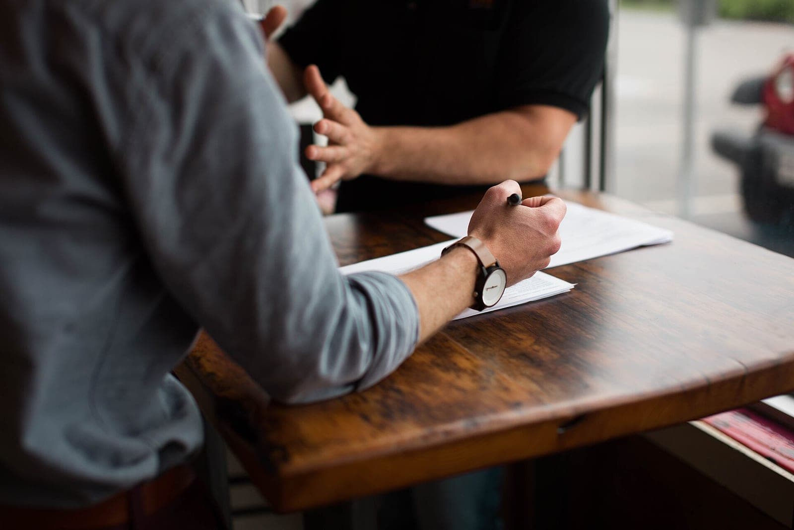 Two people at a wooden table go over printed pages, one holding a pen