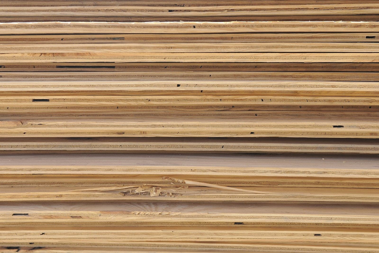 Edges of many plywood sheets stacked flat on top of one another in a wood shop
