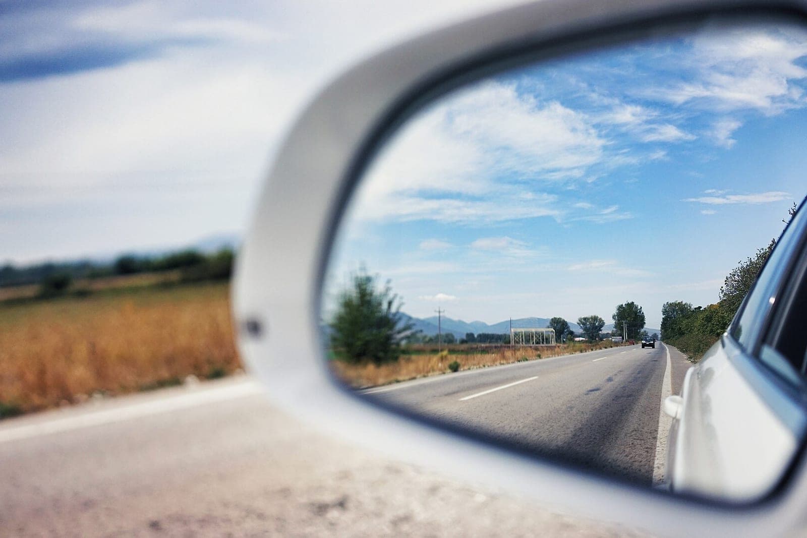 A country road reflected in the side mirror of a white car