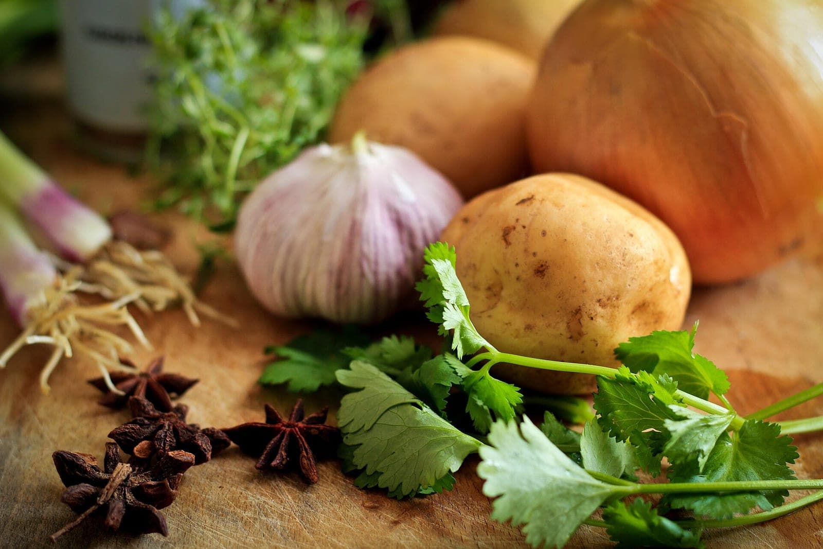 Onions, potatoes, garlic, star anise and fresh cilantro on a wooden kitchen table