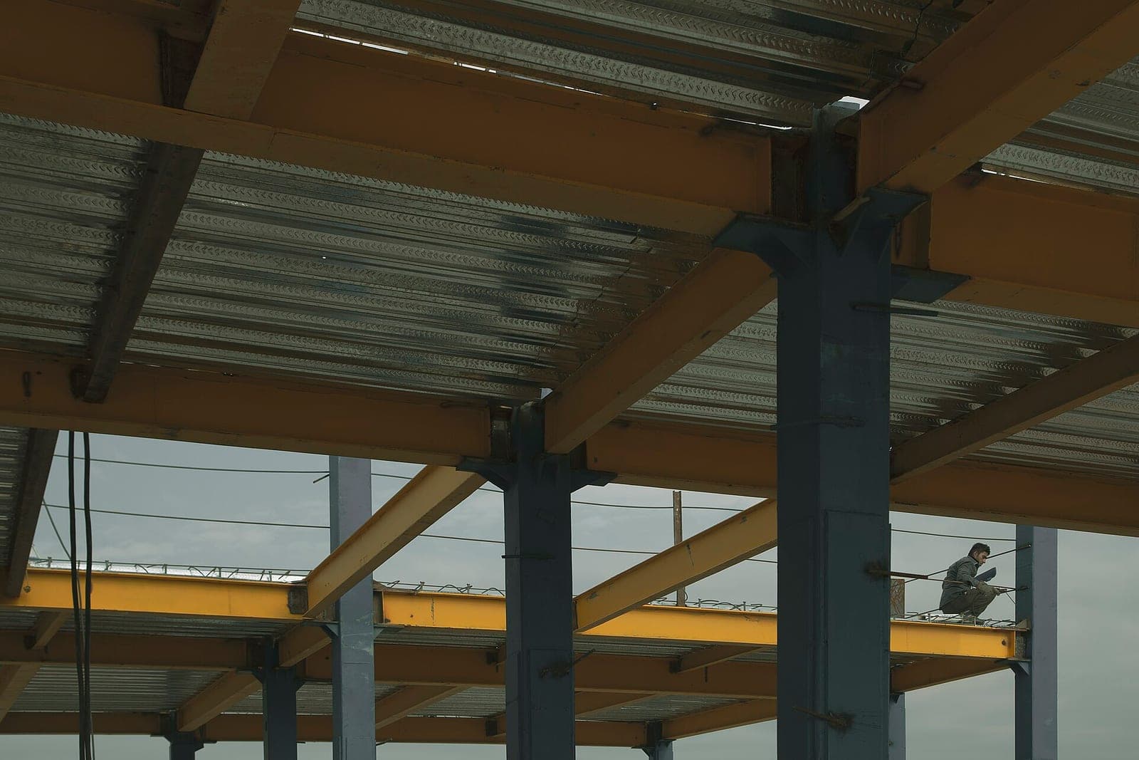 A worker crouches on a yellow steel beam under new metal floor decking in an unfinished building
