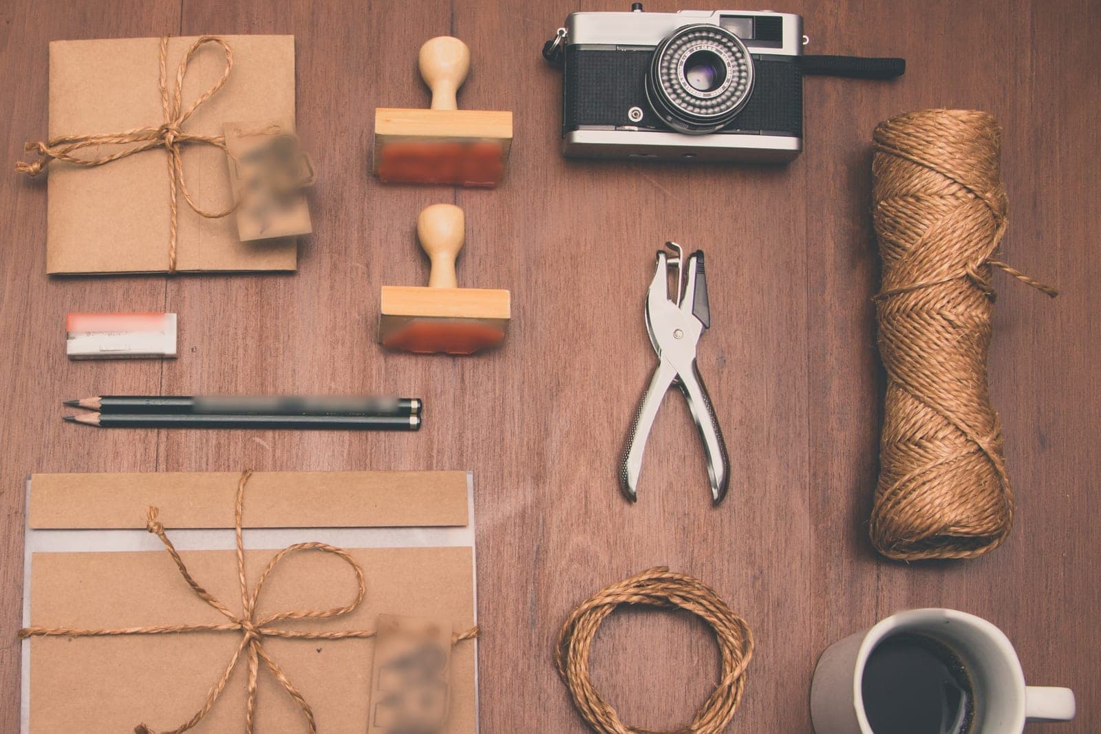 Wrapped kraft paper packets, rubber stamps, pencils, a hole punch and a camera laid out on a wooden desk
