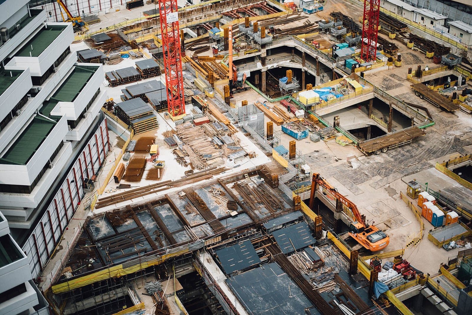 A busy construction site seen from above, with rebar mats, formwork, cranes and an orange excavator