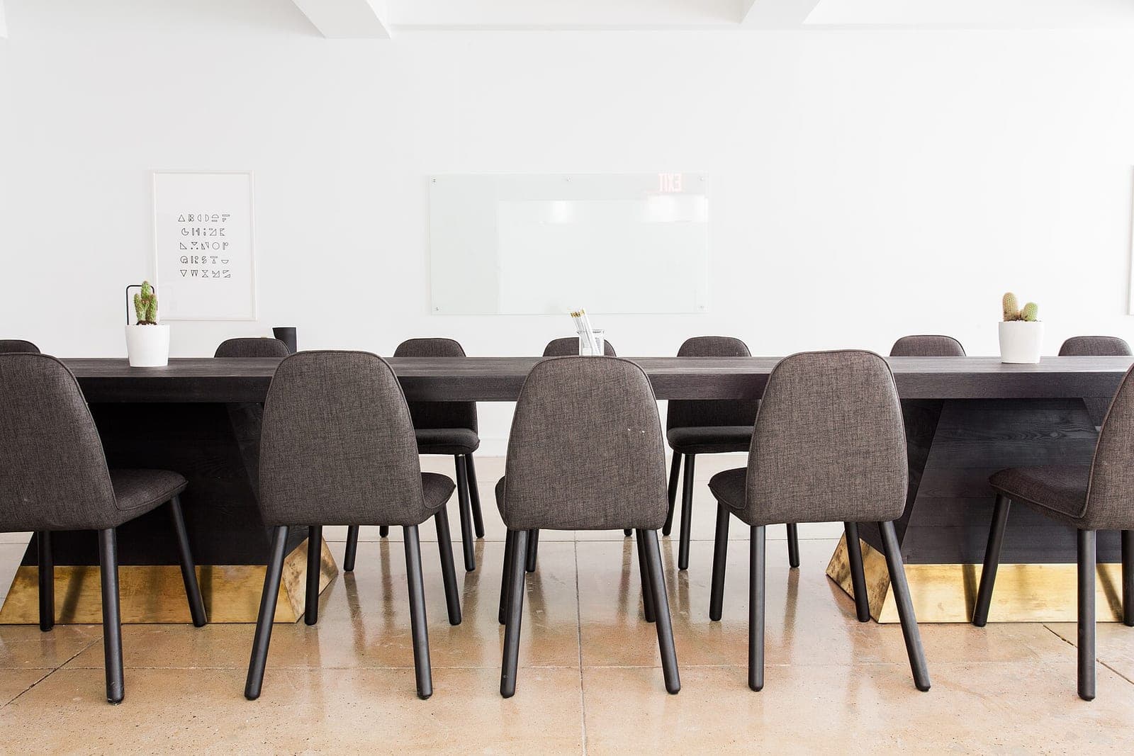 A long dark meeting table lined with gray fabric chairs in a bright white room