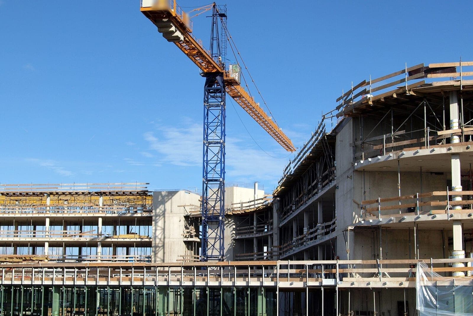 A tower crane stands beside a concrete building under construction with open floors and wooden guardrails