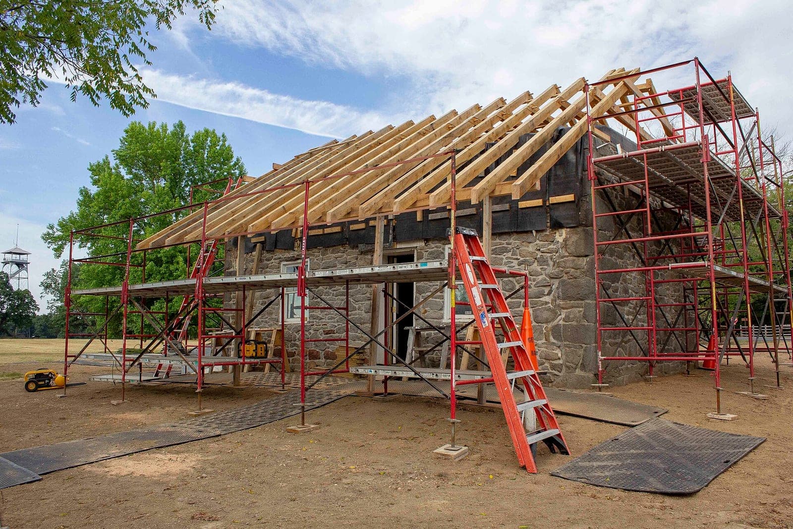 New wooden roof rafters on a small stone house, with red scaffolding and an orange ladder around it