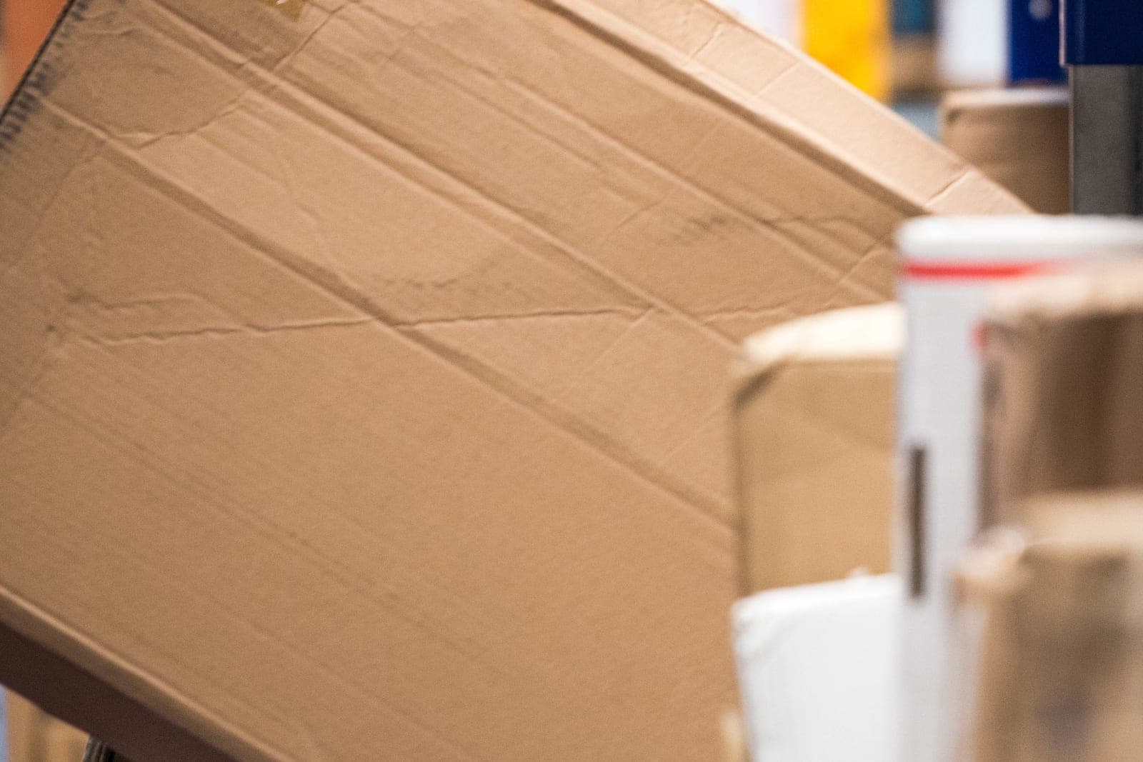 A large creased cardboard box tilts onto a shelf beside other wrapped parcels