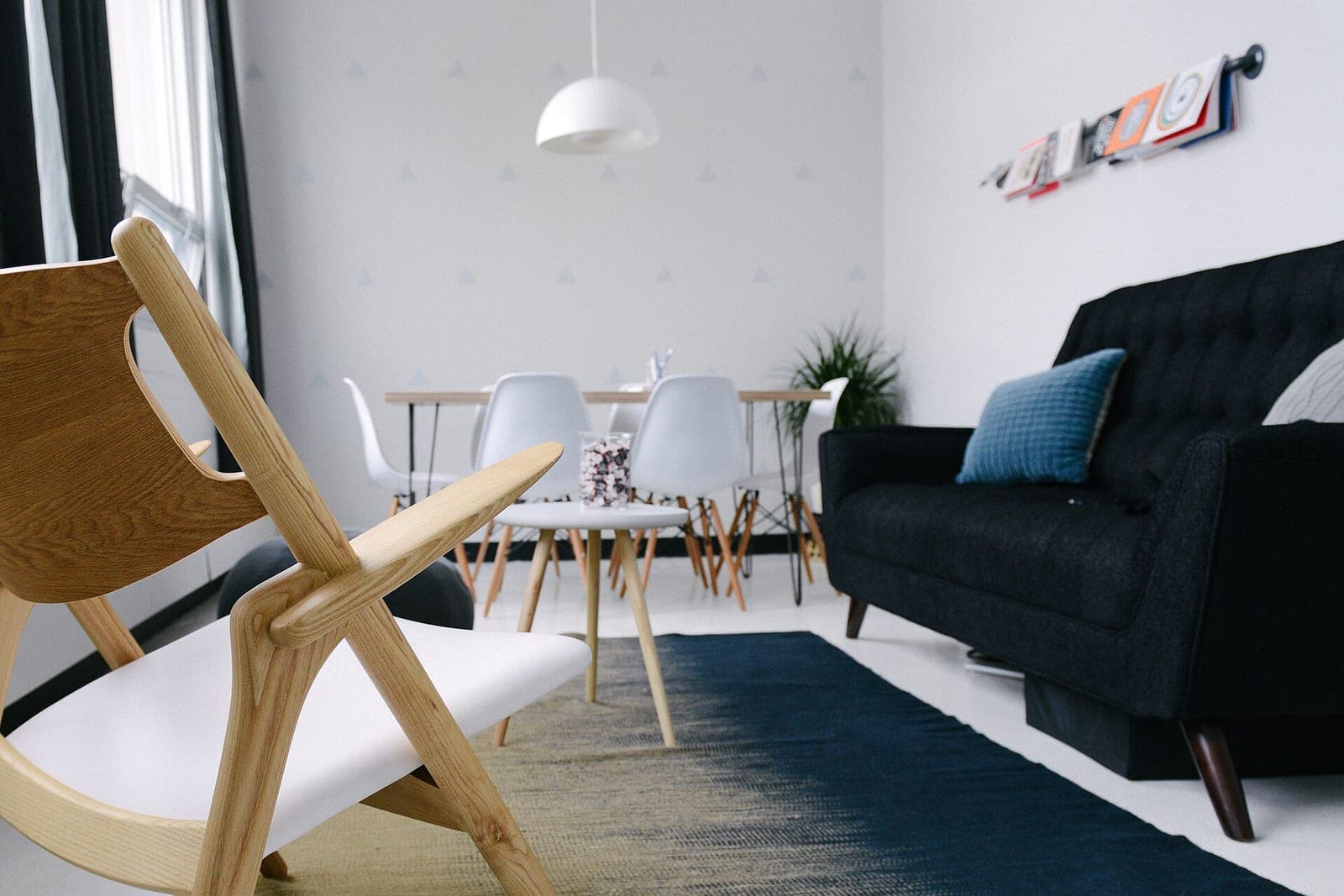 A bright office waiting area with a wooden armchair, a dark sofa, a small round table and white chairs at a table behind