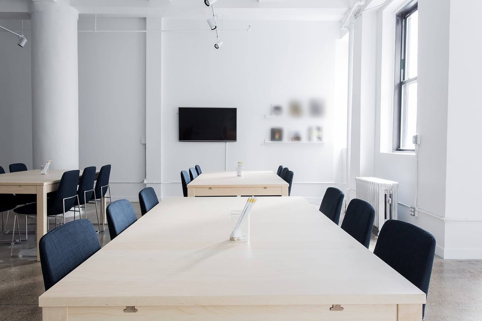 A bright, empty meeting room with long wooden tables, navy chairs and a wall screen